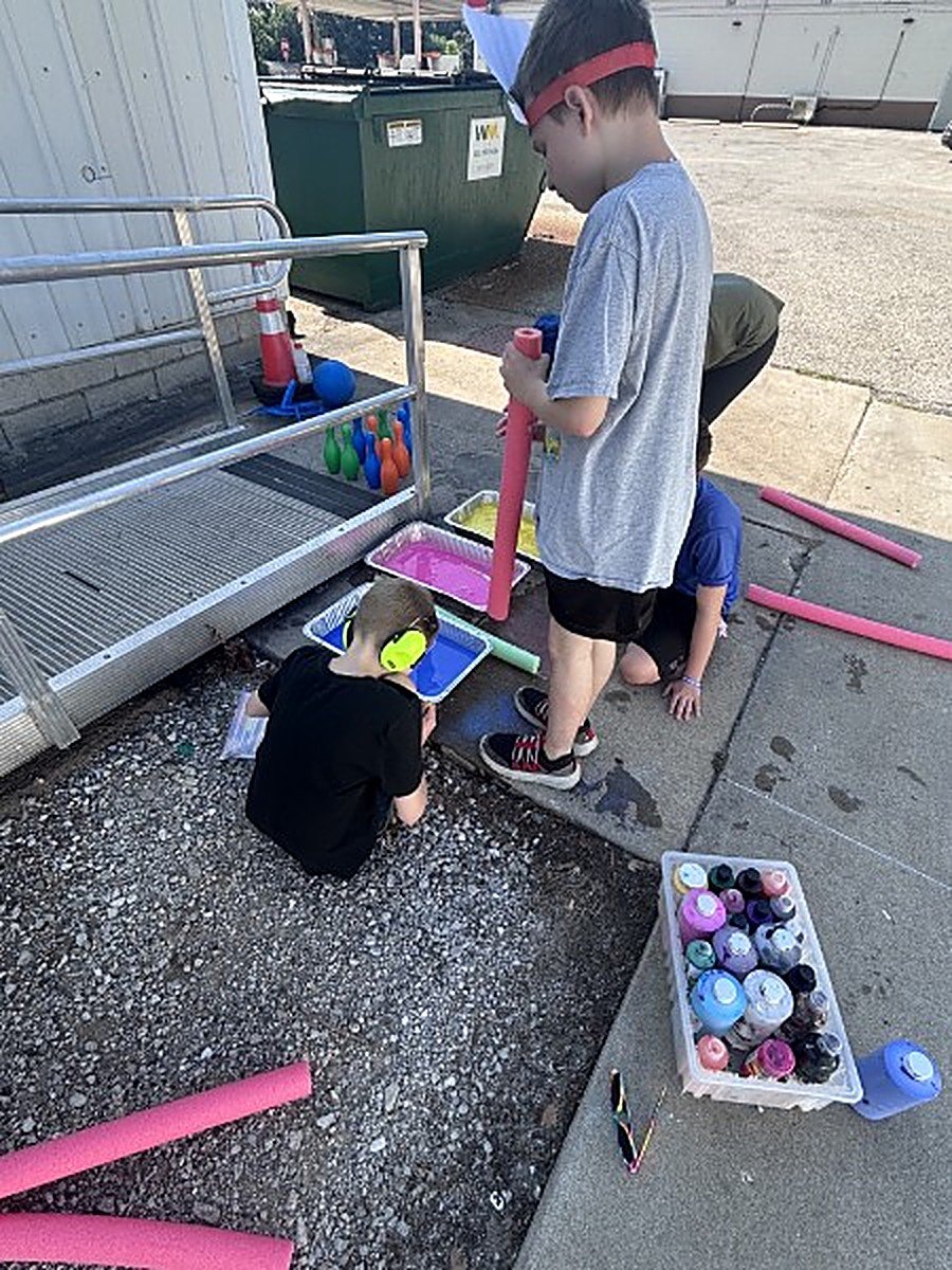 Participants painting outdoors with pool noodles and colored water