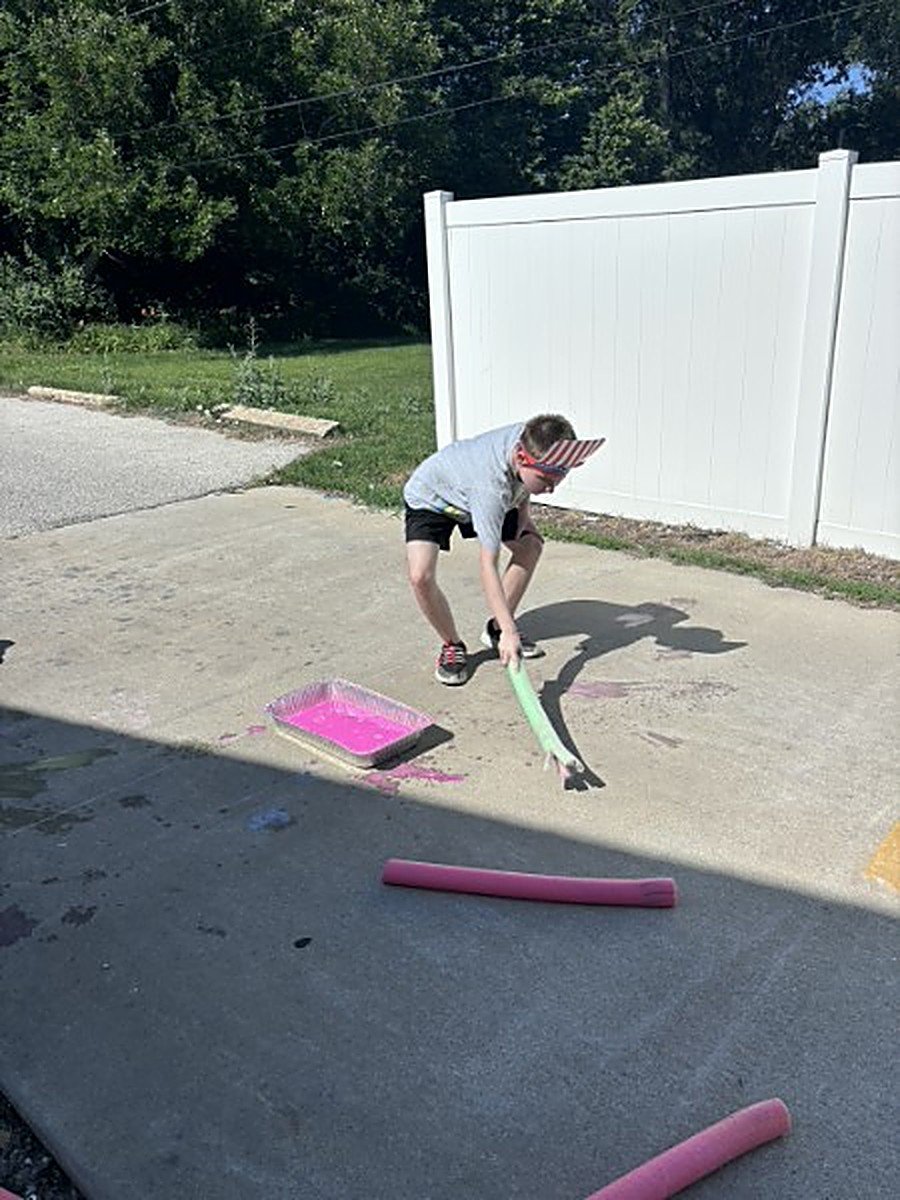 A youth painting the ground with a pool noodle and colored water